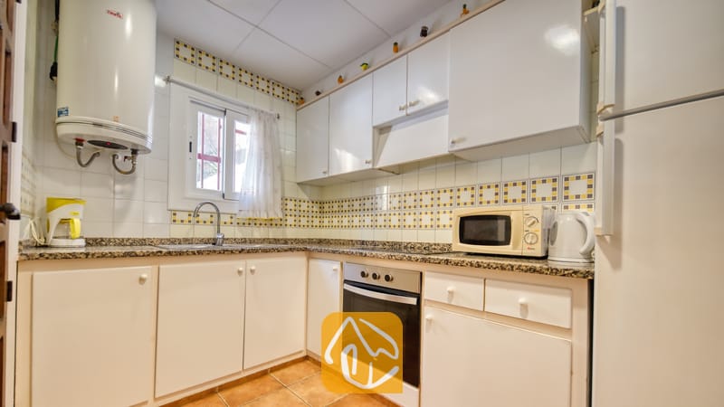 Vakantievilla's Costa Brava Spanje - Villa Blanca - Keuken voorzien van witte kasten, granieten aanrechtbladen, een inbouwoven en decoratieve gele tegels met een motief boven de gootsteen.