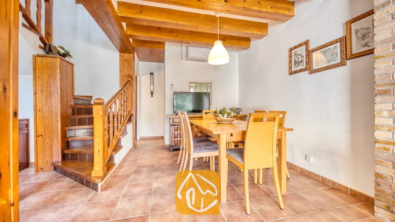 Vakantievilla's Costa Brava Spanje - Villa Blanca - Houten eettafel met bijpassende stoelen in een interieur dat wordt gekenmerkt door zichtbare plafondbalken, een tegelvloer en een houten trap.