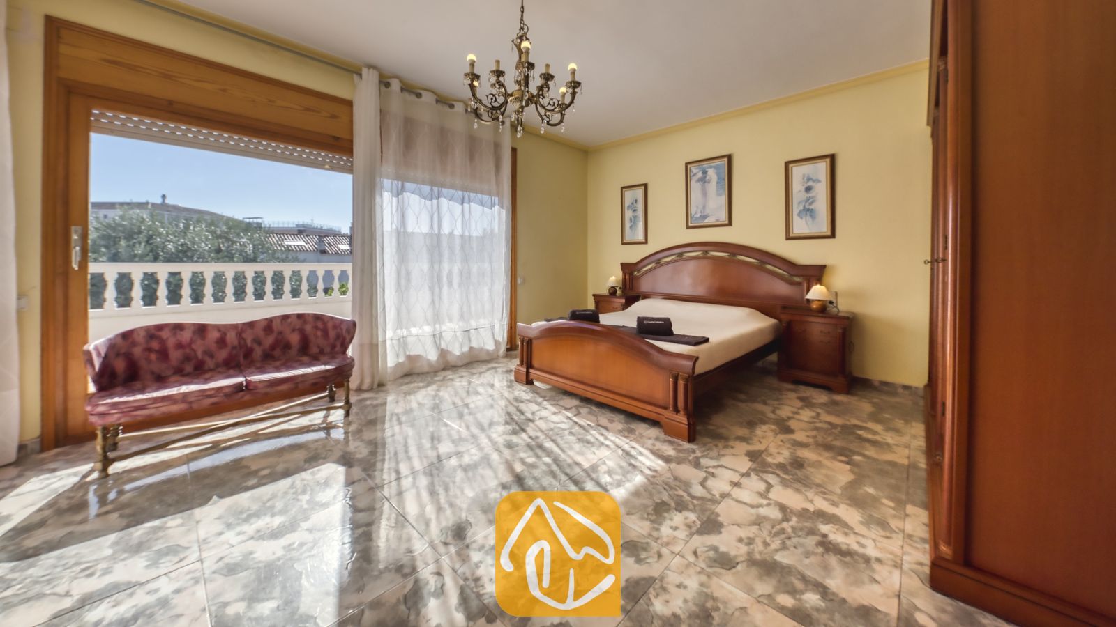 Vakantievilla's Costa Brava Spanje - Villa Baileys - Slaapkamer met een houten bedframe, geglazuurde tegels met patroon en een glazen schuifdeur die uitkomt op een zonnig balkon.