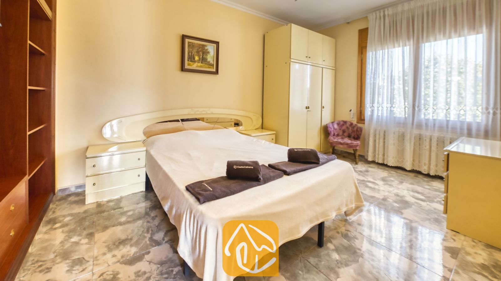 Vakantievilla's Costa Brava Spanje - Villa Baileys - Slaapkamer met een tweepersoonsbed, witte sprei, twee bij elkaar passende nachtkastjes, lichte houten kasten en een raam met in-betweens.