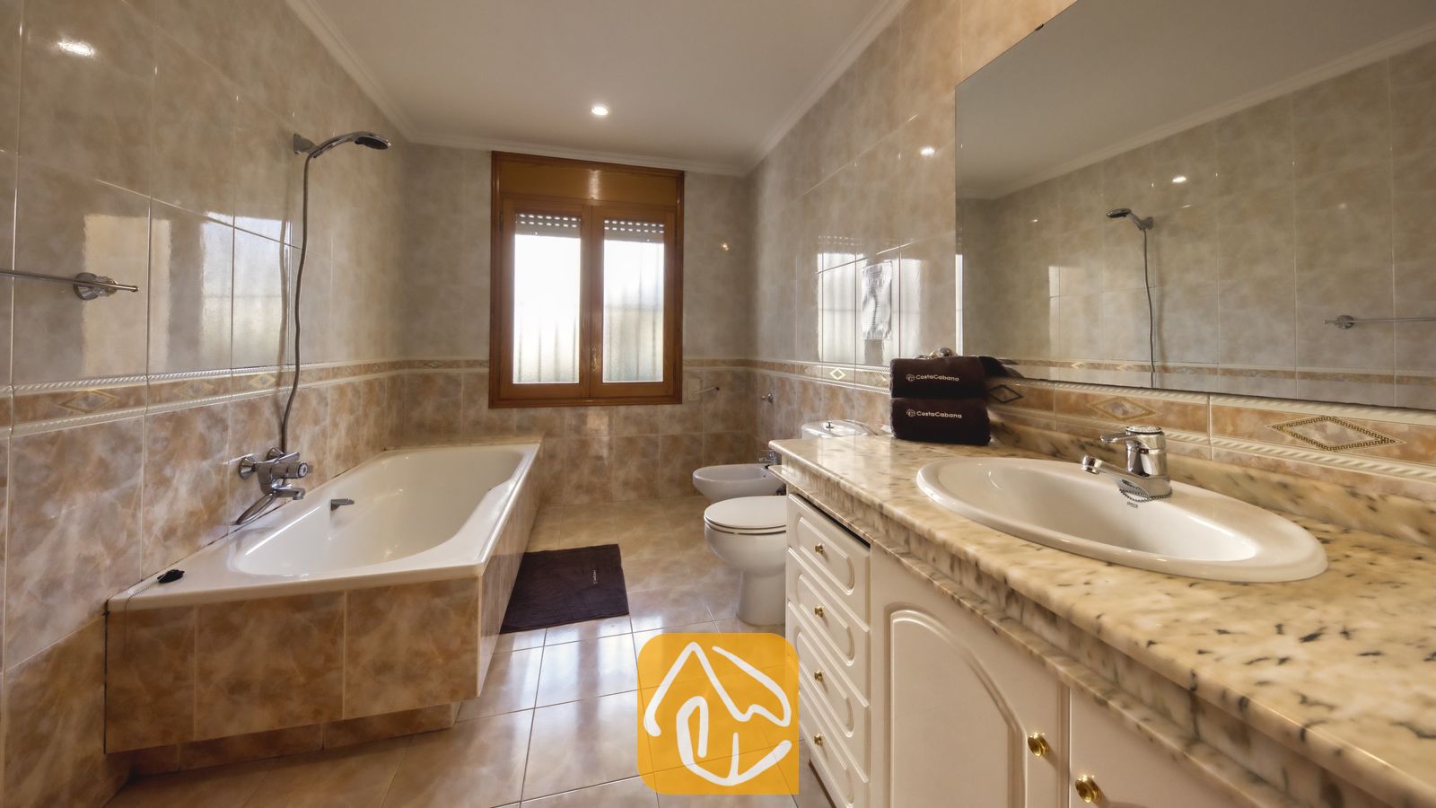 Vakantievilla's Costa Brava Spanje - Villa Baileys - Gefullyode badkamer voorzien van een wit ligbad met douchekop, een wastafelmeubel met marmeren blad en een grote wandspiegel.