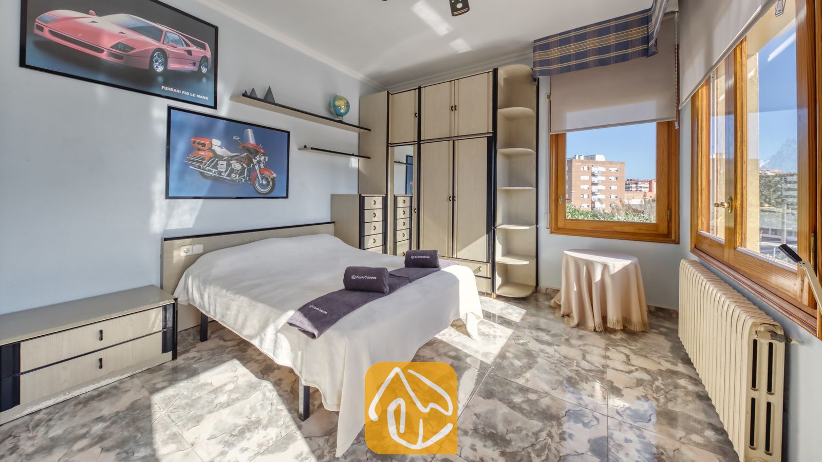 Vakantievilla's Costa Brava Spanje - Villa Baileys - Slaapkamer met een tweepersoonsbed, een grote ingebouwde houten kledingkast, marmeren vloeren en automobilia-wanddecoratie.