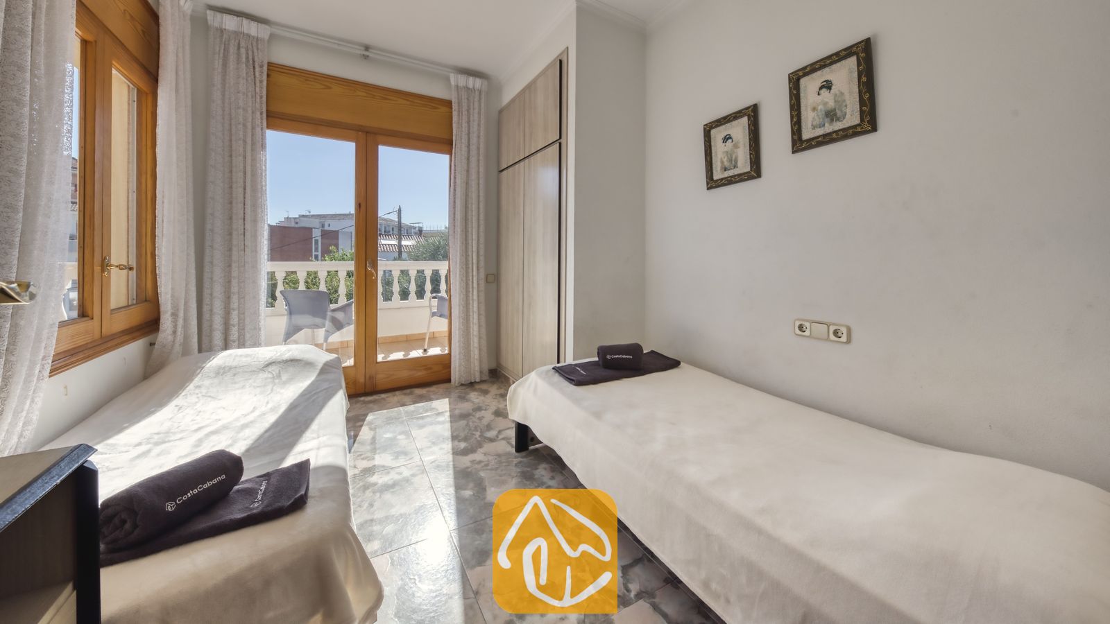 Vakantievilla's Costa Brava Spanje - Villa Baileys - Slaapkamer met twee eenpersoonsbedden, marmeren tegelvloeren, houten deur- en raamkozijnen en toegang tot een balkon.