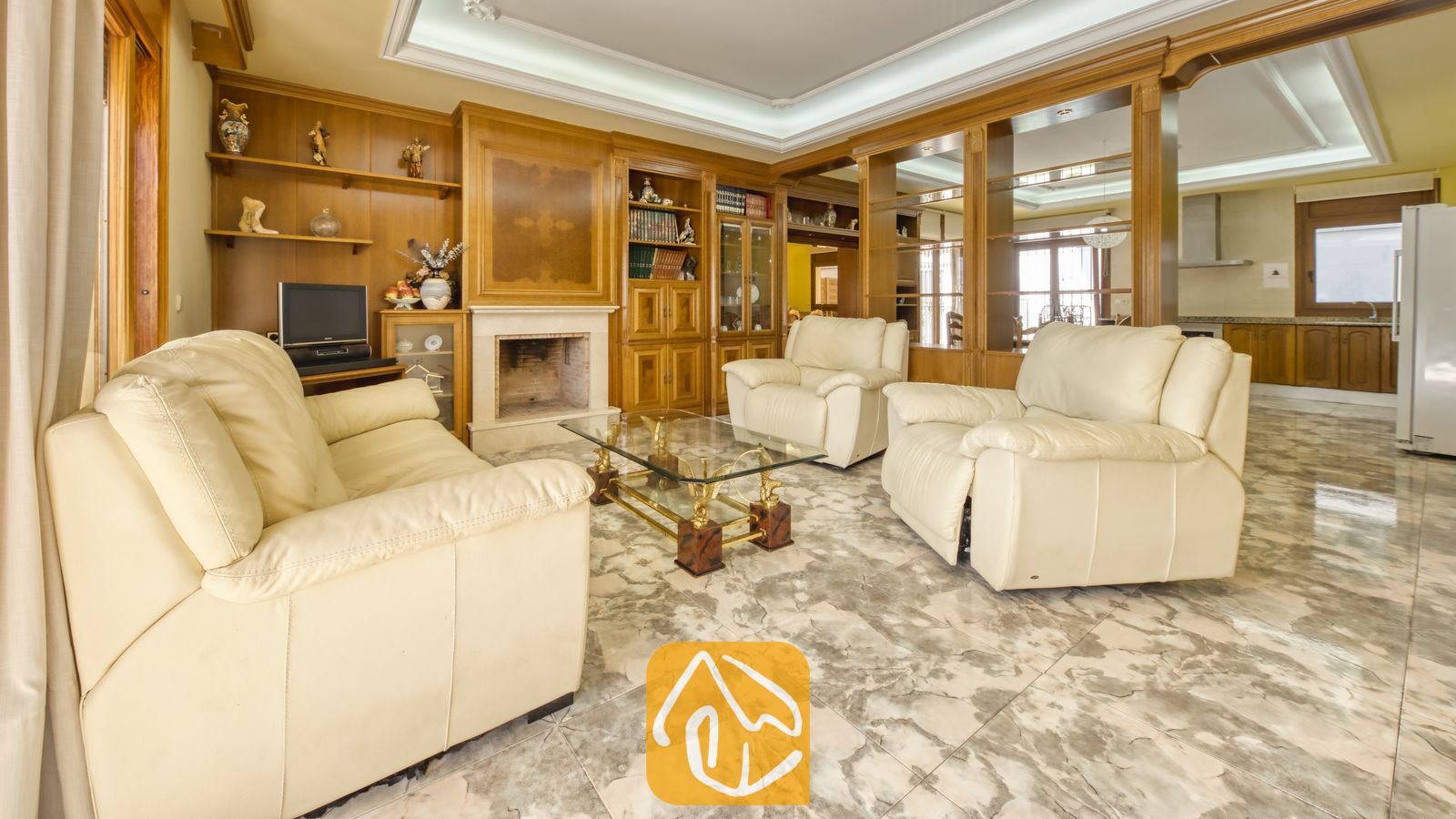 Vakantievilla's Costa Brava Spanje - Villa Baileys - Woonkamer met crèmekleurige leren banken, marmeren vloeren, een glazen salontafel, ingebouwde houten wandkasten en een stenen open haard.