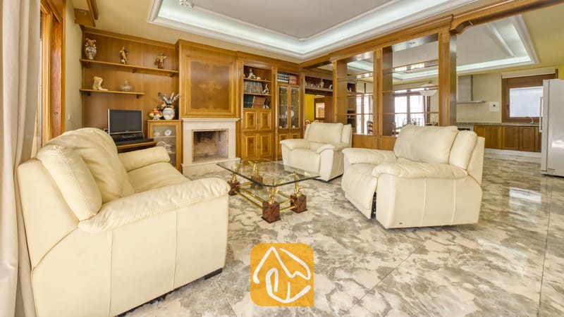 Vakantievilla's Costa Brava Spanje - Villa Baileys - Woonkamer met crèmekleurige leren banken, marmeren vloeren, een glazen salontafel, ingebouwde houten wandkasten en een stenen open haard.