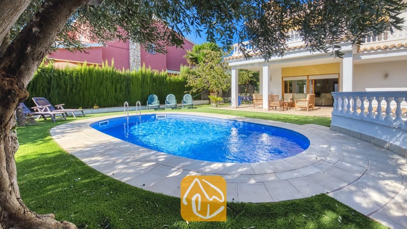 Vakantievilla's Costa Brava Spanje - Villa Baileys - Oval zwembad met blauw water en betegelde rand bij Villa Baileys, voorzien van ligstoelen op het gras en een overdekt terras op de achtergrond.