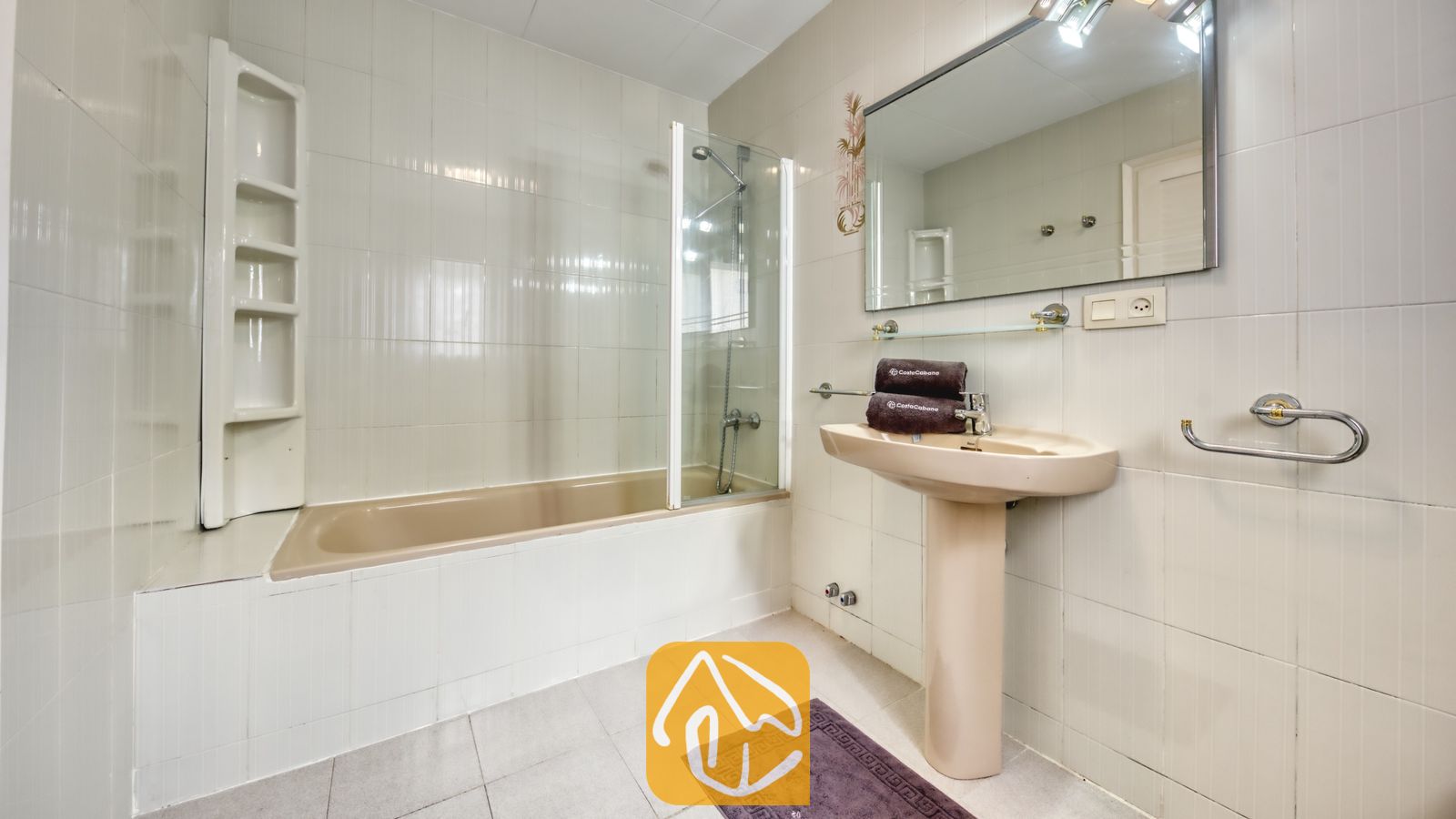 Vakantievilla's Costa Brava Spanje - Villa Miro - De badkamer van Villa Miro is voorzien van een beige ligbad met een glazen douchescherm, een wastafel op zuil en wit betegelde muren.