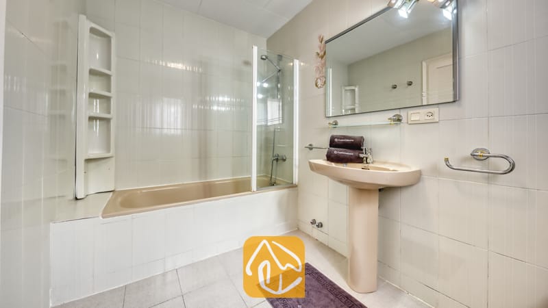 Villas de vacances Costa Brava Espagne - Villa Miro - Salle de bain de la Villa Miro dotée d'une baignoire beige avec paroi vitrée, d'un lavabo sur colonne et d'un carrelage mural blanc.