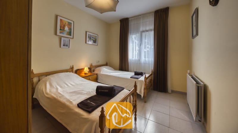 Villas de vacances Costa Brava Espagne - Villa Miro - Chambre avec deux lits simples en bois à la Villa Miro, agrémentée de linge de maison blanc, de serviettes brun foncé, d'une lampe de chevet et d'un radiateur blanc.