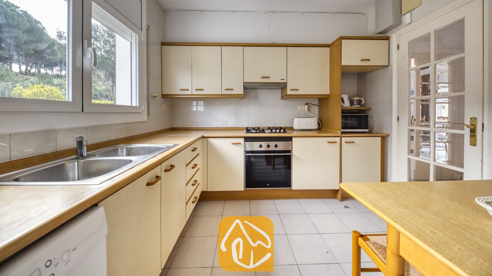 Vakantievilla's Costa Brava Spanje - Villa Miro - De keuken van Villa Miro is voorzien van crèmekleurige kasten met houten afwerking, een dubbele roestvrijstalen spoelbak en inbouwapparatuur, waaronder een oven en een gaskookplaat.