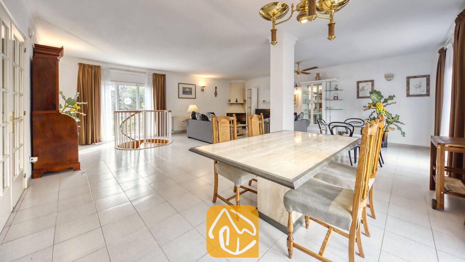Vakantievilla's Costa Brava Spanje - Villa Miro - Eethoek in Villa Miro met een tafel met stenen blad, houten stoelen, wit betegelde vloeren en een wenteltrap die leidt naar een woonkamer met gestreepte banken.