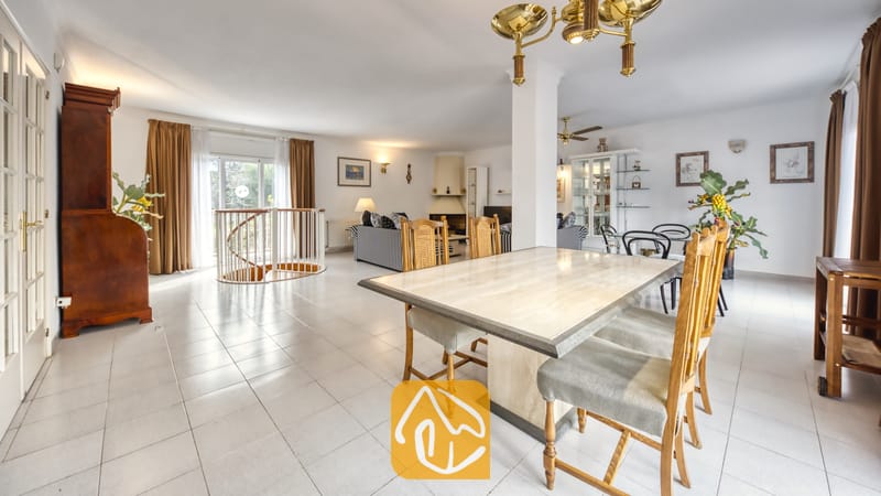 Vakantievilla's Costa Brava Spanje - Villa Miro - Eethoek in Villa Miro met een tafel met stenen blad, houten stoelen, wit betegelde vloeren en een wenteltrap die leidt naar een woonkamer met gestreepte banken.