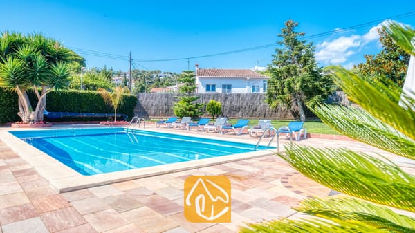 Vakantievilla's Costa Brava Spanje - Villa Miro - Privézwembad bij Villa Miro met helderblauw water, omringd door een terras van natuursteen, ligstoelen en tropische palmbomen onder een strakblauwe lucht.