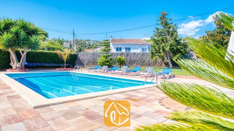 Vakantievilla's Costa Brava Spanje - Villa Miro - Privézwembad bij Villa Miro met helderblauw water, omringd door een terras van natuursteen, ligstoelen en tropische palmbomen onder een strakblauwe lucht.
