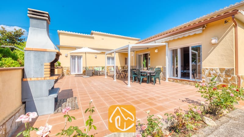 Vakantievilla's Costa Brava Spanje - Villa Miro - Op het betegelde terras van Villa Miro bevindt zich een ingebouwde stenen barbecue, compleet met een eethoek onder een pergola en een comfortabele loungehoek met een witte parasol.