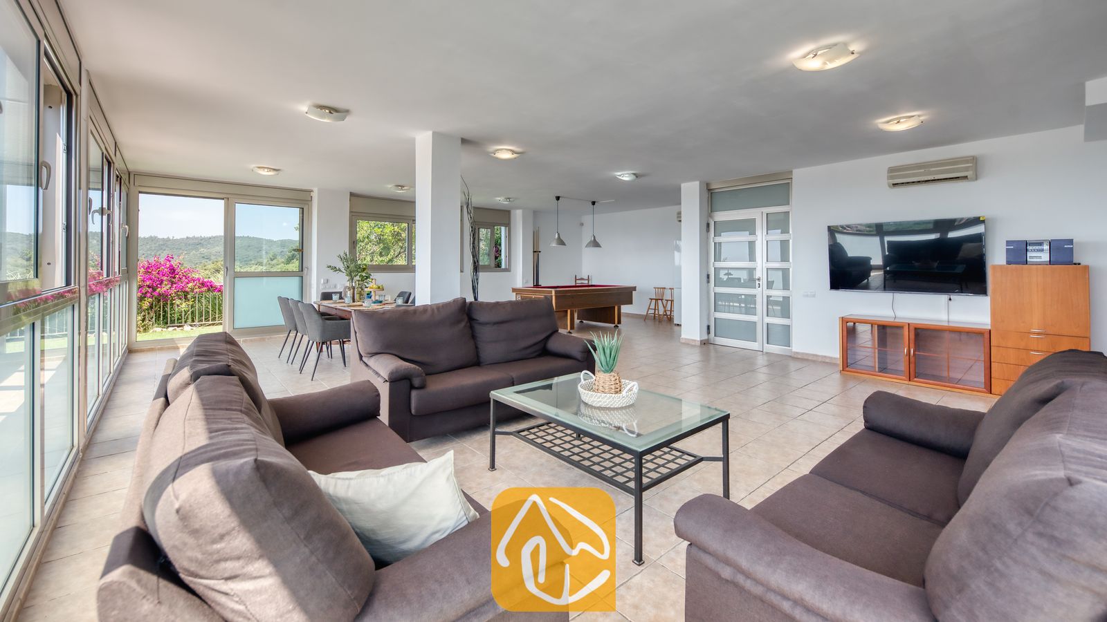 Vakantievilla's Costa Brava Spanje - Villa Sandy Beach - Woonkamer van Villa Sandy Beach met donkerbruine banken, een glazen salontafel en een pooltafel in een open ruimte met plavuizenvloeren.