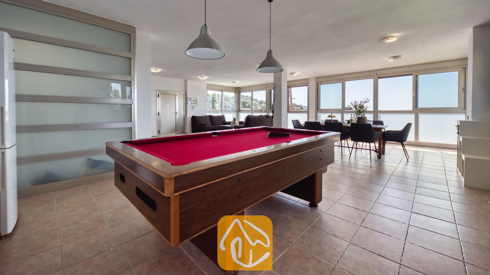 Vakantievilla's Costa Brava Spanje - Villa Sandy Beach - Een pooltafel met rood laken en grijze hanglampen in de open woonruimte van Villa Sandy Beach, voorzien van een tegelvloer en een eethoek bij de grote raampartijen.
