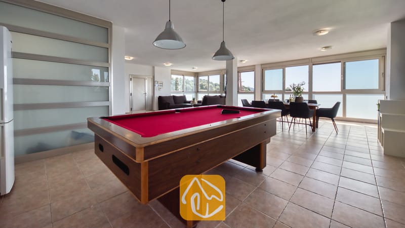 Vakantievilla's Costa Brava Spanje - Villa Sandy Beach - Een pooltafel met rood laken en grijze hanglampen in de open woonruimte van Villa Sandy Beach, voorzien van een tegelvloer en een eethoek bij de grote raampartijen.