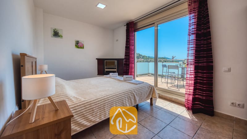 Villas de vacances Costa Brava Espagne - Villa Sandy Beach - Chambre à la Villa Sandy Beach dotée d'un lit double, de sols carrelés et de grandes baies vitrées coulissantes s'ouvrant sur une terrasse avec salon de jardin et vue sur les collines verdoyantes.