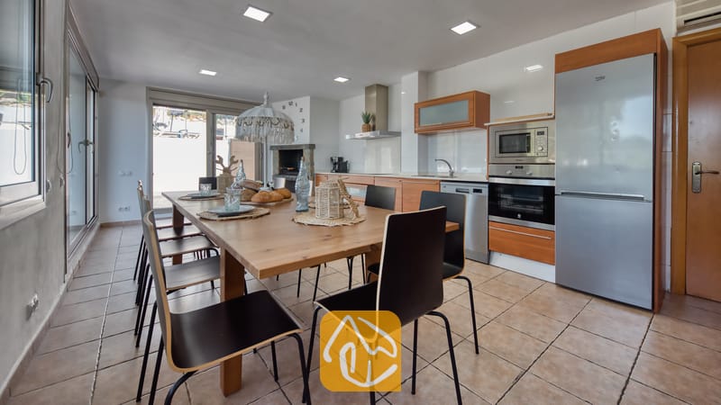 Vakantievilla's Costa Brava Spanje - Villa Sandy Beach - De keuken en eethoek van Villa Sandy Beach zijn voorzien van een grote houten tafel met zwarte stoelen, roestvrijstalen apparatuur en een neutrale tegelvloer.