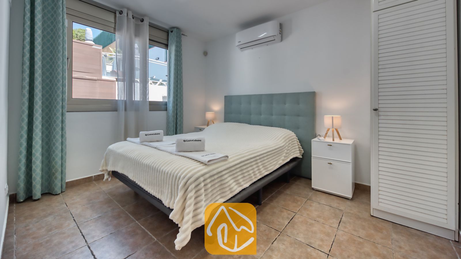 Vakantievilla's Costa Brava Spanje - Villa Sandy Beach - Slaapkamer in Villa Sandy Beach, voorzien van een tweepersoonsbed met een getuft hoofdbord in zeegroene tint, witte nachtkastjes met bijpassende lampen en een wandgemonteerde airconditioning.