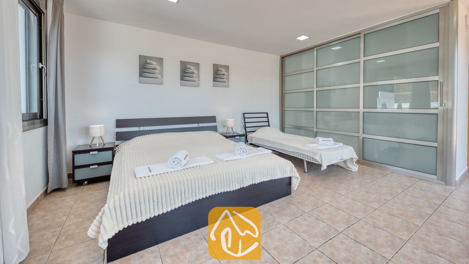 Vakantievilla's Costa Brava Spanje - Villa Sandy Beach - Slaapkamer in Villa Sandy Beach, voorzien van een tweepersoonsbed met geribbeld crèmekleurig beddengoed, een eenpersoons logeerbed en een grote schuifdeurkast van matglas op een tegelvloer.