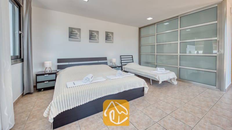 Villas de vacances Costa Brava Espagne - Villa Sandy Beach - Chambre à la Villa Sandy Beach équipée d'un lit double avec une parure de lit crème côtelée, d'un lit simple d'appoint et d'une grande armoire à portes coulissantes en verre dépoli, le tout sur un sol carrelé.