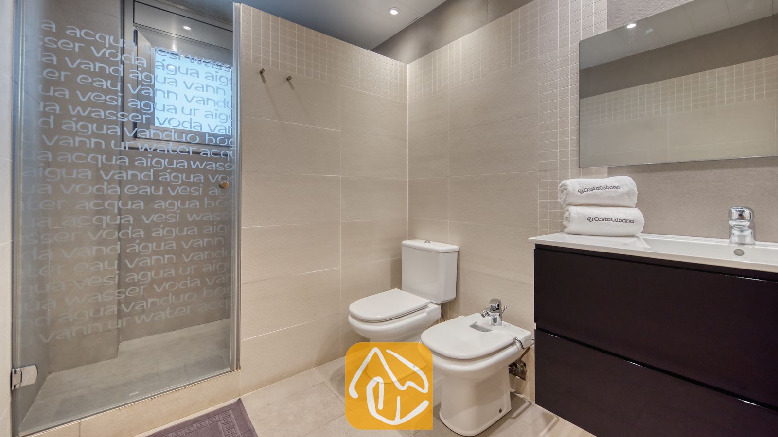 Vakantievilla's Costa Brava Spanje - Villa Sandy Beach - Badkamer voorzien van een inloopdouche met matglas, wit toilet en bidet, en een donker wastafelmeubel met een witte wastafel en een grote spiegel.