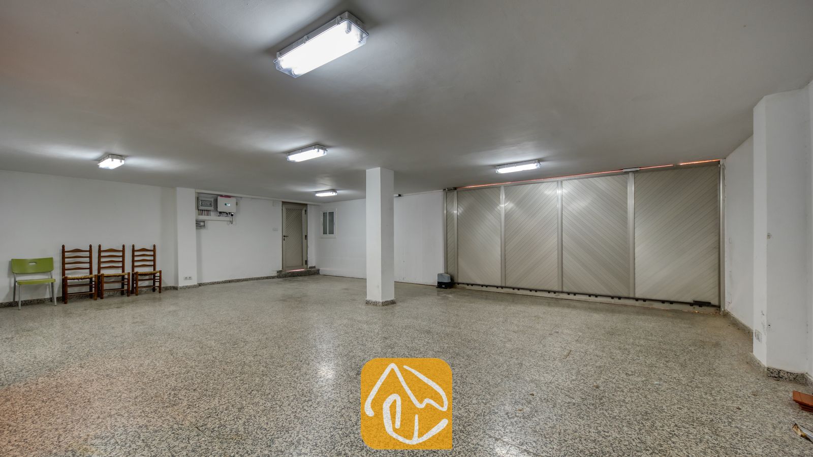 Vakantievilla's Costa Brava Spanje - Villa Sandy Beach - Ruime garage bij Villa Sandy Beach, voorzien van een gespikkelde terrazzovloer, witte muren en een grote metalen schuifdeur.