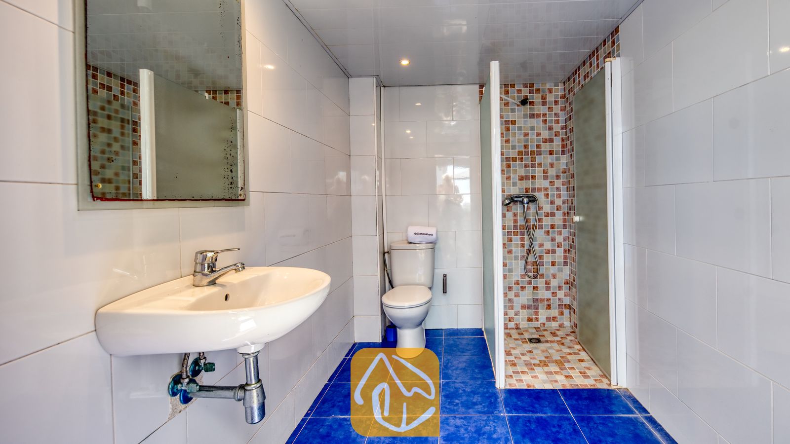 Vakantievilla's Costa Brava Spanje - Villa Sandy Beach - Badkamer met blauwe vloertegels, een witte wastafel aan de muur en een inloopdouche met veelkleurige mozaïektegels.