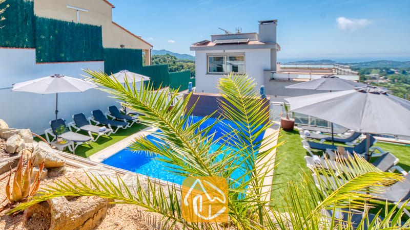 Vakantievilla's Costa Brava Spanje - Villa Sandy Beach - Buitenzwembad bij Villa Sandy Beach met grijze ligbedden op een groen gazon, witte parasols en een weids uitzicht op de kust onder een strakblauwe lucht.