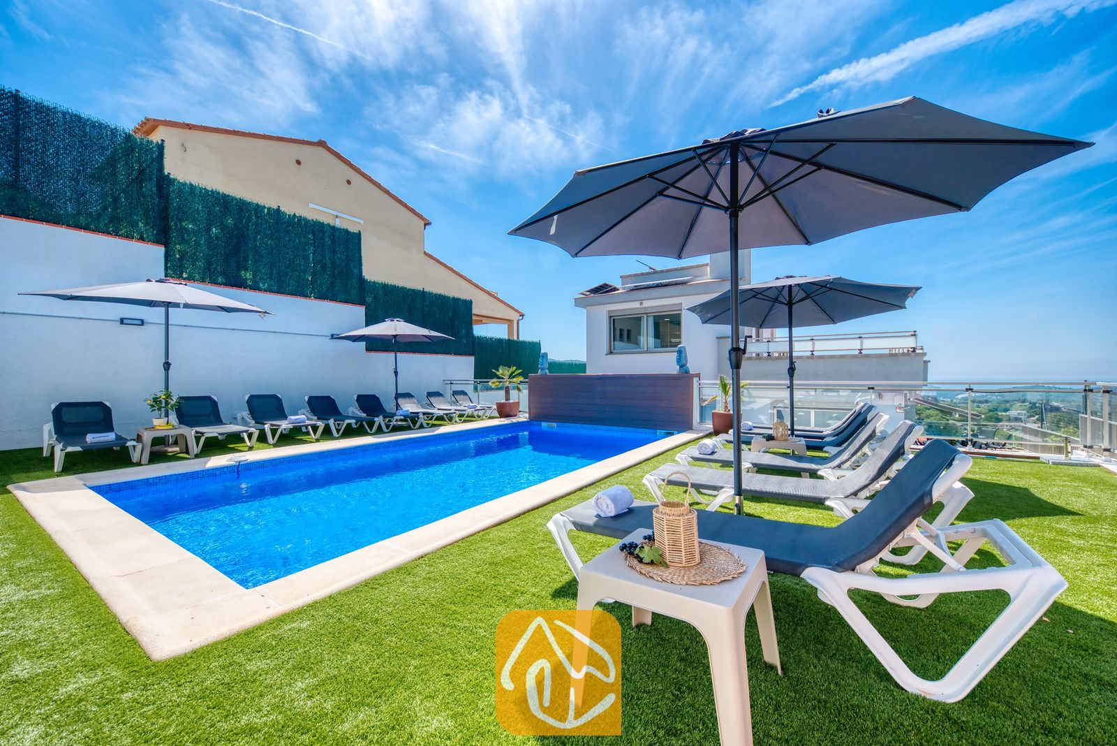Vakantievilla's Costa Brava Spanje - Villa Sandy Beach - Privézwembad bij Villa Sandy Beach, omringd door kunstgras, grijze ligbedden met witte frames en grote parasols onder een strakblauwe lucht.