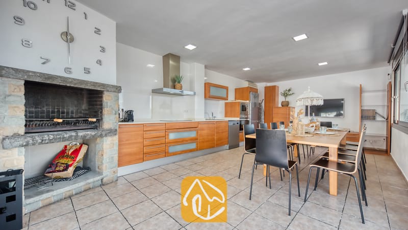 Vakantievilla's Costa Brava Spanje - Villa Sandy Beach - Binnenbarbecue van natuursteen en een moderne keuken in Villa Sandy Beach, voorzien van houten kasten, een eettafel met zwarte stoelen en een tegelvloer.
