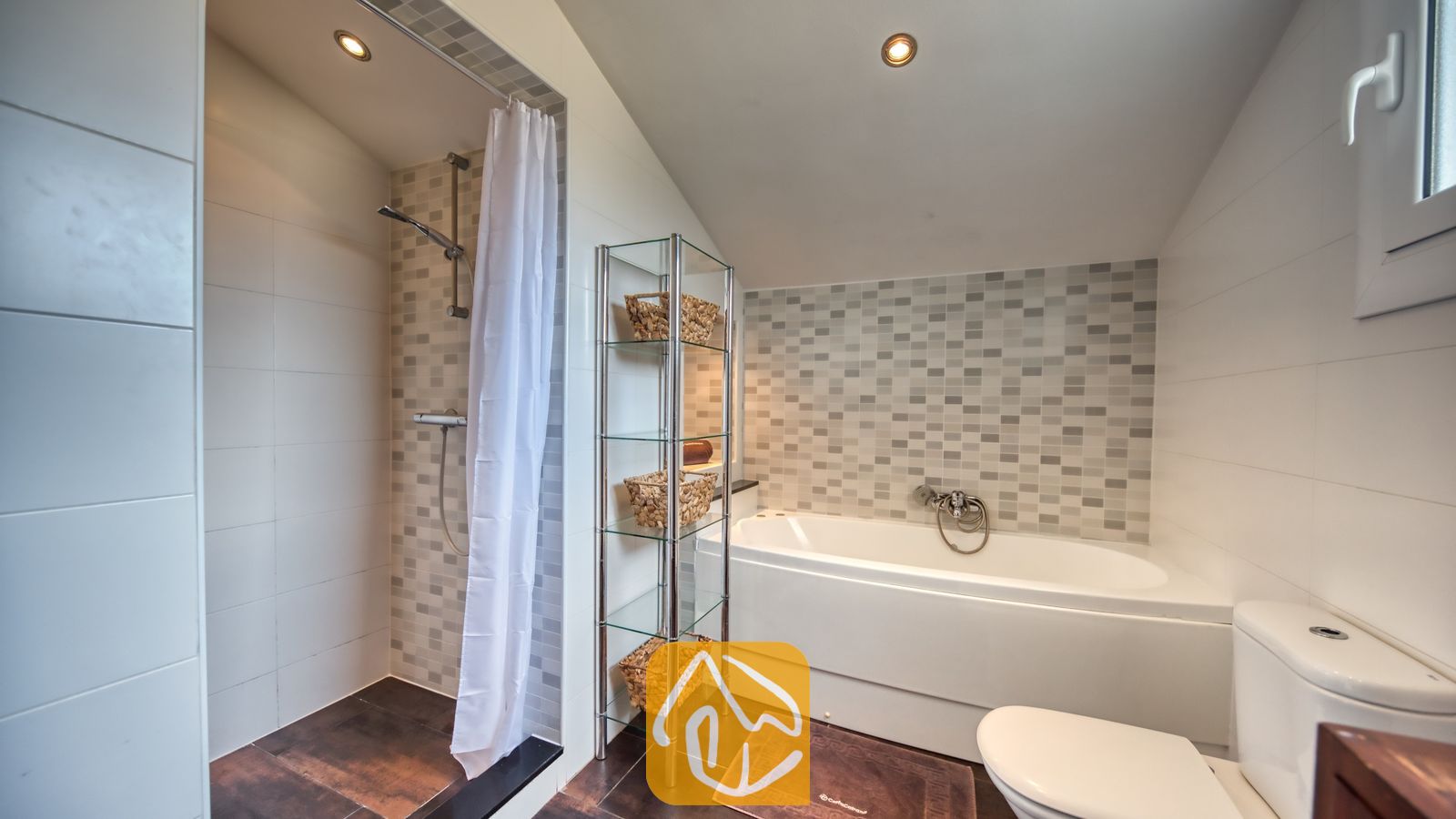 Vakantievilla's Costa Brava Spanje - Villa Madonna - Moderne badkamer met een betegelde inloopdouche met een wit douchegordijn, een wit ligbad, een glazen wandrek met geweven manden en een toilet.