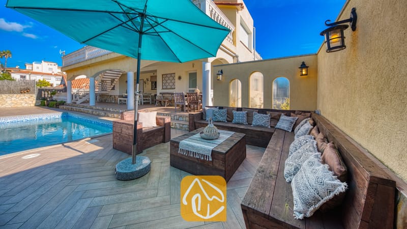 Vakantievilla's Costa Brava Spanje - Villa Madonna - Houten buitenloungehoek met bedrukte kussens en een grote blauwe parasol bij het zwembad van Villa Madonna.