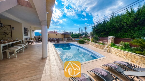 Vakantievilla's Costa Brava Spanje - Villa Madonna - Privézwembad en betegeld terras bij Villa Madonna, voorzien van vier ligbedden en een overdekte eethoek buiten onder een helderblauwe hemel.