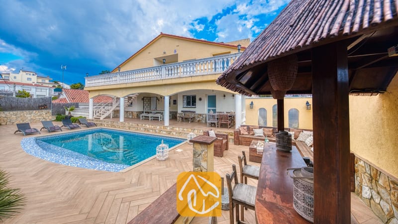 Vakantievilla's Costa Brava Spanje - Villa Madonna - Buitenkant van Villa Madonna met een zwembad, betegeld terras en een overdekte buitenbar met houten zitmeubelen onder een rieten dak.