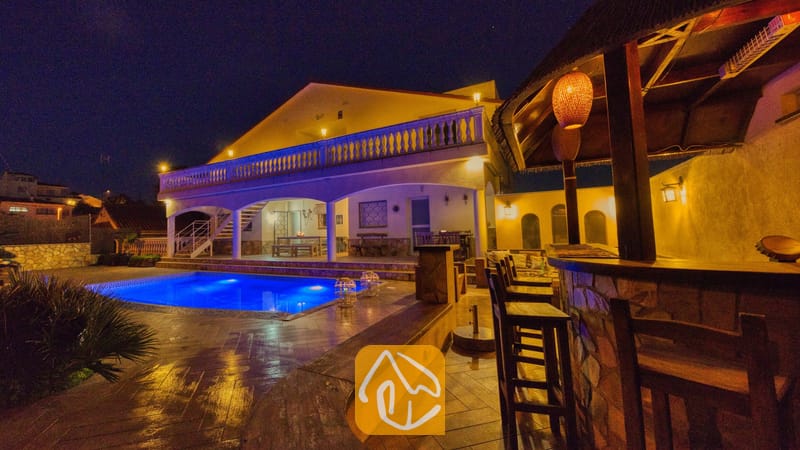 Villas de vacances Costa Brava Espagne - Villa Madonna - Extérieur de la Villa Madonna de nuit, mettant en valeur une piscine illuminée, un bar extérieur couvert avec des tabourets en bois, ainsi qu'une terrasse éclairée dotée d'une balustrade.