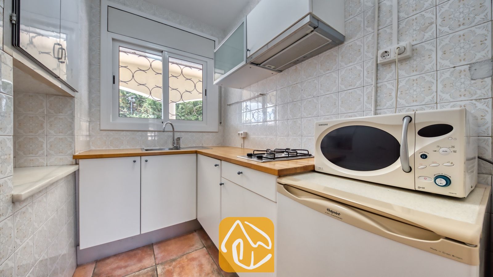Vakantievilla's Costa Brava Spanje - Villa Madonna - Kookhoek met witte kasten, houten werkbladen, een gaskookplaat, magnetron en een raam voorzien van dievenklauwen.