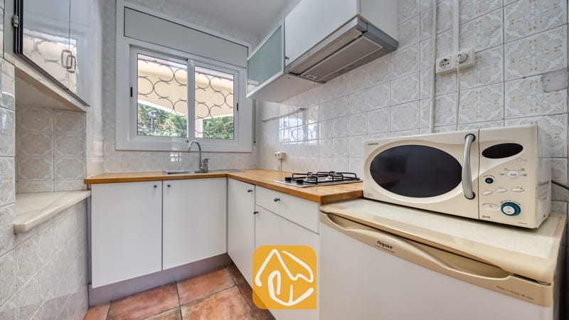 Villas de vacances Costa Brava Espagne - Villa Madonna - Coin cuisine aménagé avec des placards blancs, des plans de travail en bois, une plaque de cuisson au gaz, un four à micro-ondes et une fenêtre pourvue de barreaux de sécurité.