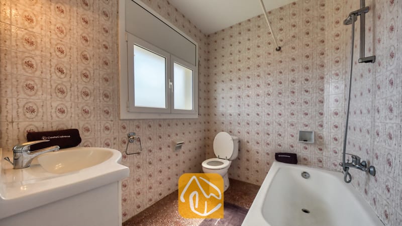 Villas de vacances Costa Brava Espagne - Villa Madonna - Salle de bains dotée de murs en céramique à motifs, d'un lavabo blanc, d'une baignoire avec douche verticale et de toilettes situées sous une fenêtre en verre dépoli.