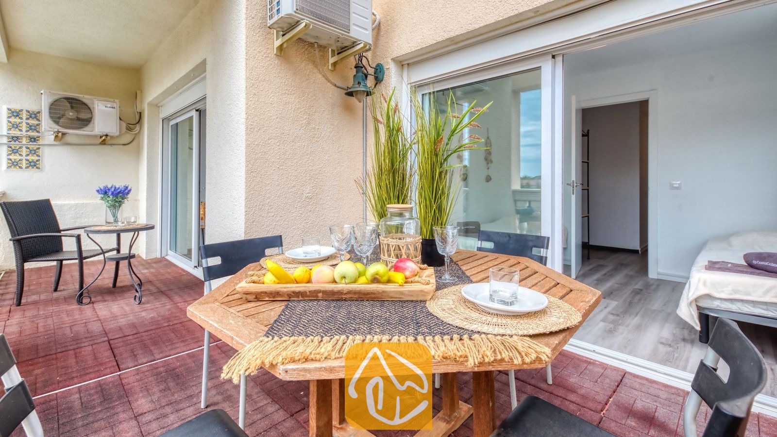 Vakantievilla's Costa Brava Spanje - Villa Madonna - Houten eettafel voor buiten op een balkon met een schaal fruit, glazen en een pot met siergras, buiten Villa Madonna.