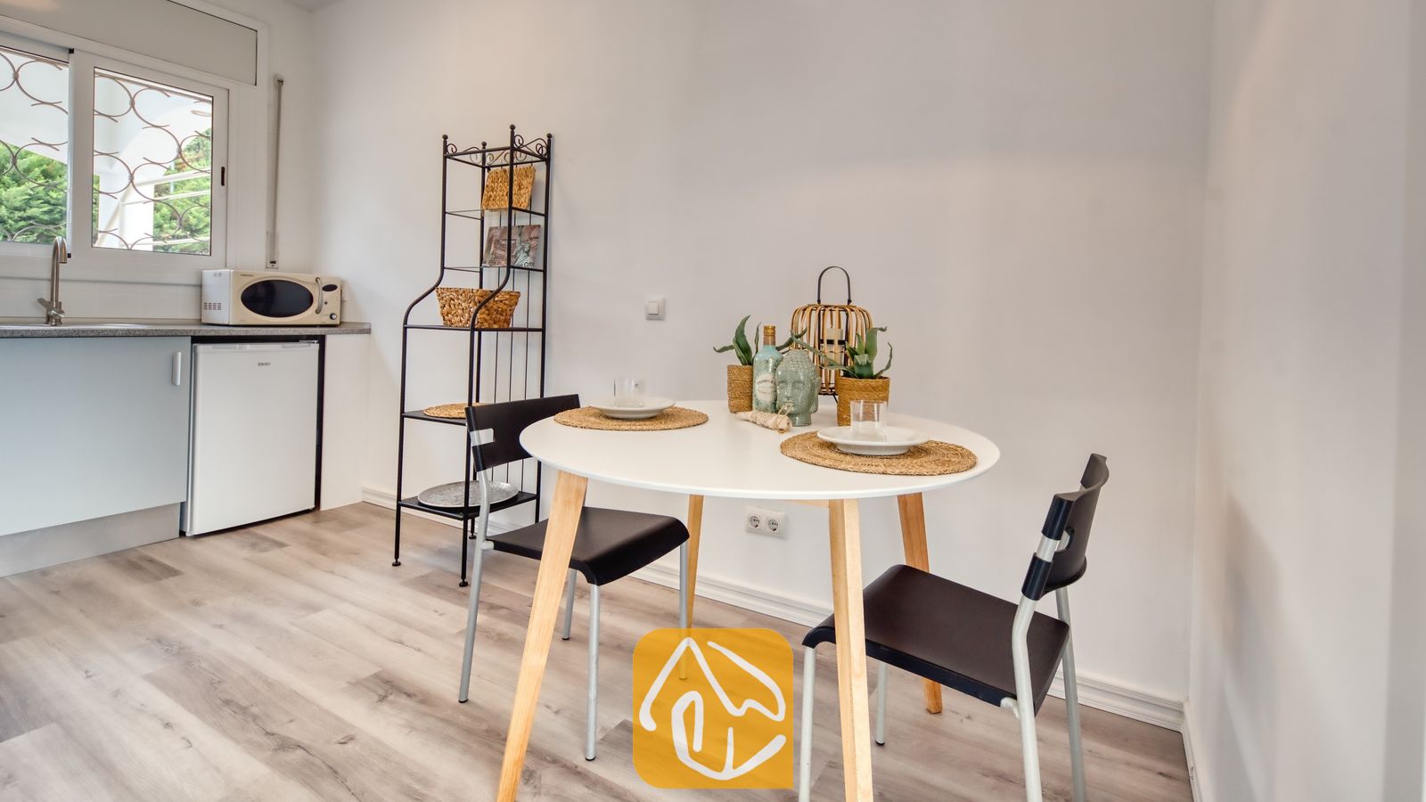 Vakantievilla's Costa Brava Spanje - Villa Madonna - Ronde witte eettafel met houten poten en twee zwarte stoelen, gedekt met geweven placemats en glaswerk in de keuken van Villa Madonna.