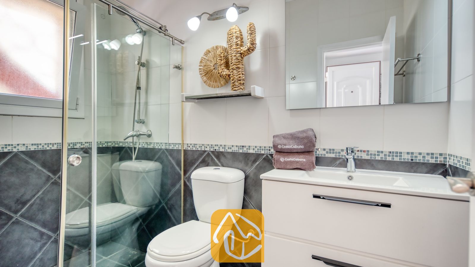 Vakantievilla's Costa Brava Spanje - Villa Madonna - Moderne badkamer met een glazen douchecabine, een wit wastafelmeubel, toilet en geweven wanddecoratie.