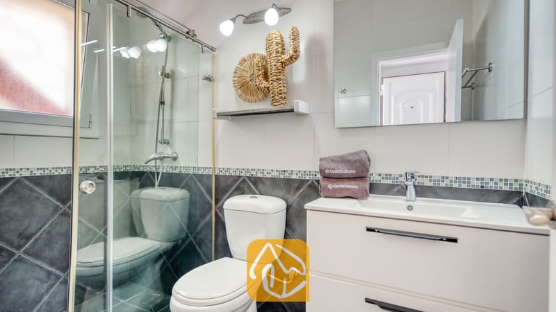 Villas de vacances Costa Brava Espagne - Villa Madonna - Salle de bains moderne comprenant une douche vitrée, un meuble-lavabo blanc, des toilettes et une décoration murale tissée.