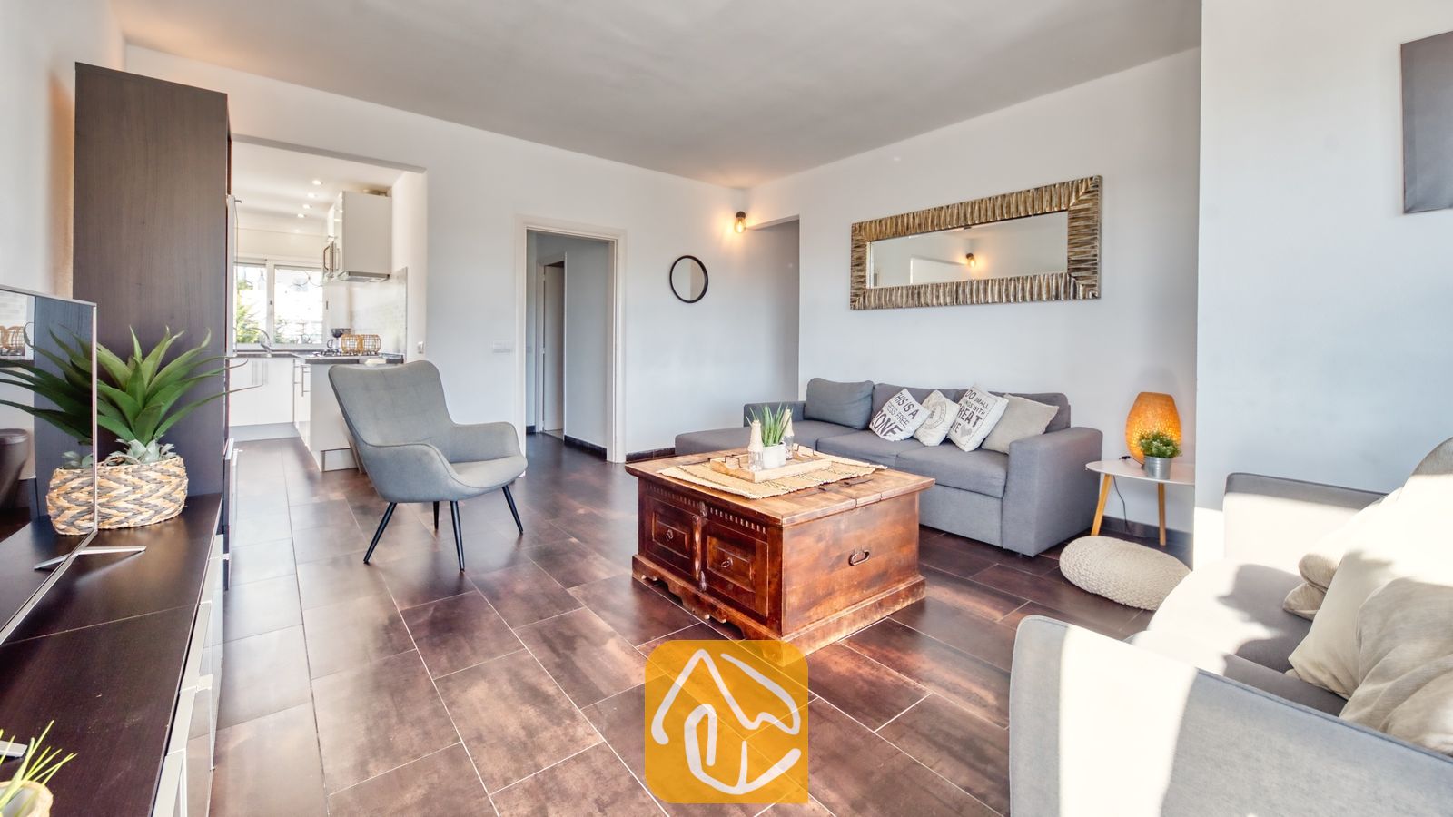 Vakantievilla's Costa Brava Spanje - Villa Madonna - Woonkamer van Villa Madonna met een grijze bank, een salontafel van donkerhout, een fauteuil en tegelvloeren, met uitzicht op de keuken.