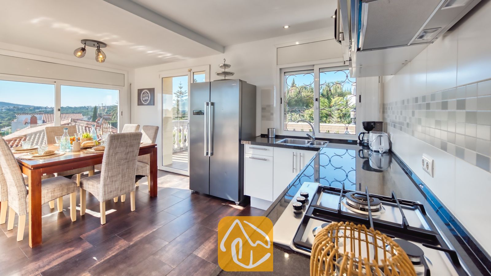 Vakantievilla's Costa Brava Spanje - Villa Madonna - Moderne keuken en eethoek in Villa Madonna met donkere aanrechtbladen, roestvrijstalen apparatuur en een houten eettafel met gestoffeerde stoelen.