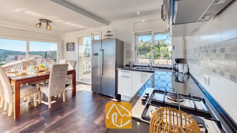 Villas de vacances Costa Brava Espagne - Villa Madonna - Cuisine moderne et coin repas de la Villa Madonna, dotés de comptoirs sombres, d'appareils en acier inoxydable et d'une table à manger en bois dressée avec des chaises rembourrées.