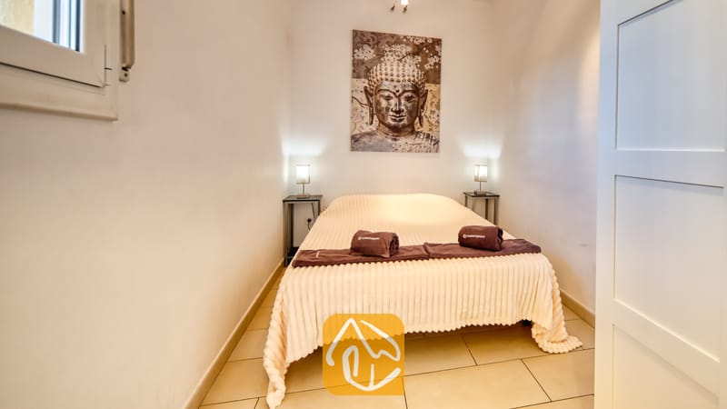 Villas de vacances Costa Brava Espagne - Villa Madonna - Chambre à coucher dotée d'un lit double avec un couvre-lit côtelé de couleur claire, de serviettes brunes enroulées et d'une grande tenture murale représentant un Bouddha au-dessus.