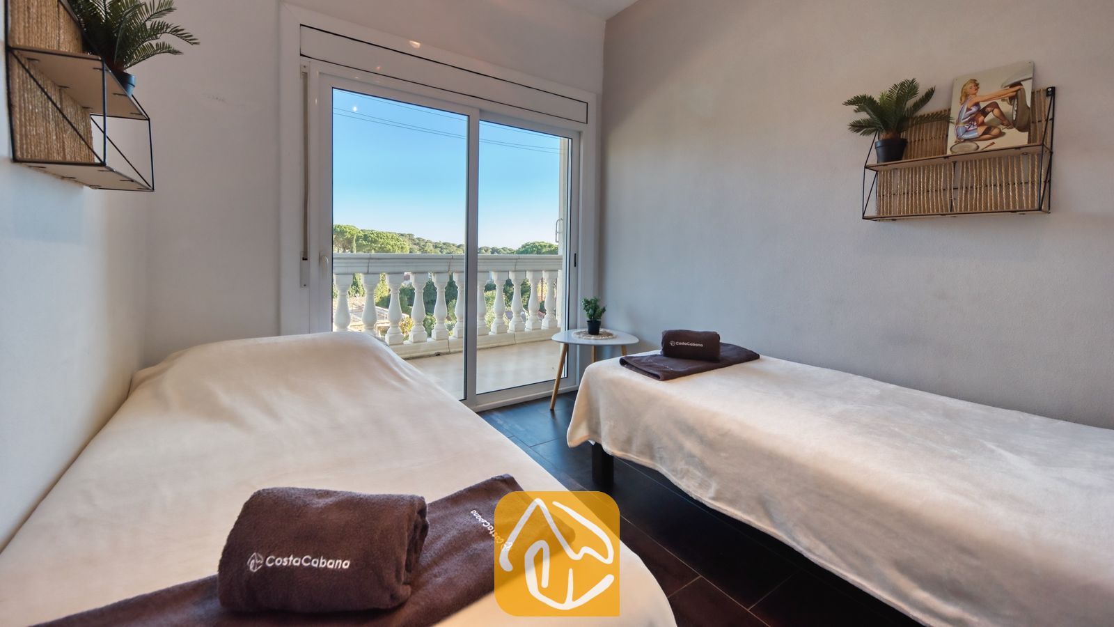 Vakantievilla's Costa Brava Spanje - Villa Madonna - Slaapkamer met twee eenpersoonsbedden, voorzien van wit beddengoed, bruine handdoeken met merklogo en een schuifpui die toegang biedt tot een balkon.